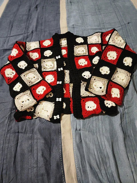 Crocheted skull granny squares sweater with a pattern of red, white, and black squares on a gray fabric background
