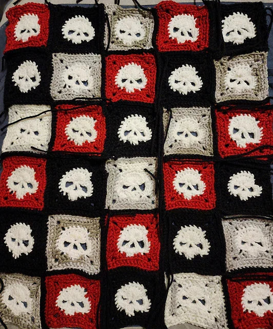 Crocheted granny square with skull patterns in red, black, and gray squares.