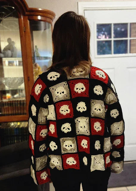 Person wearing a colorful crochet skull-patterned sweater in a room.