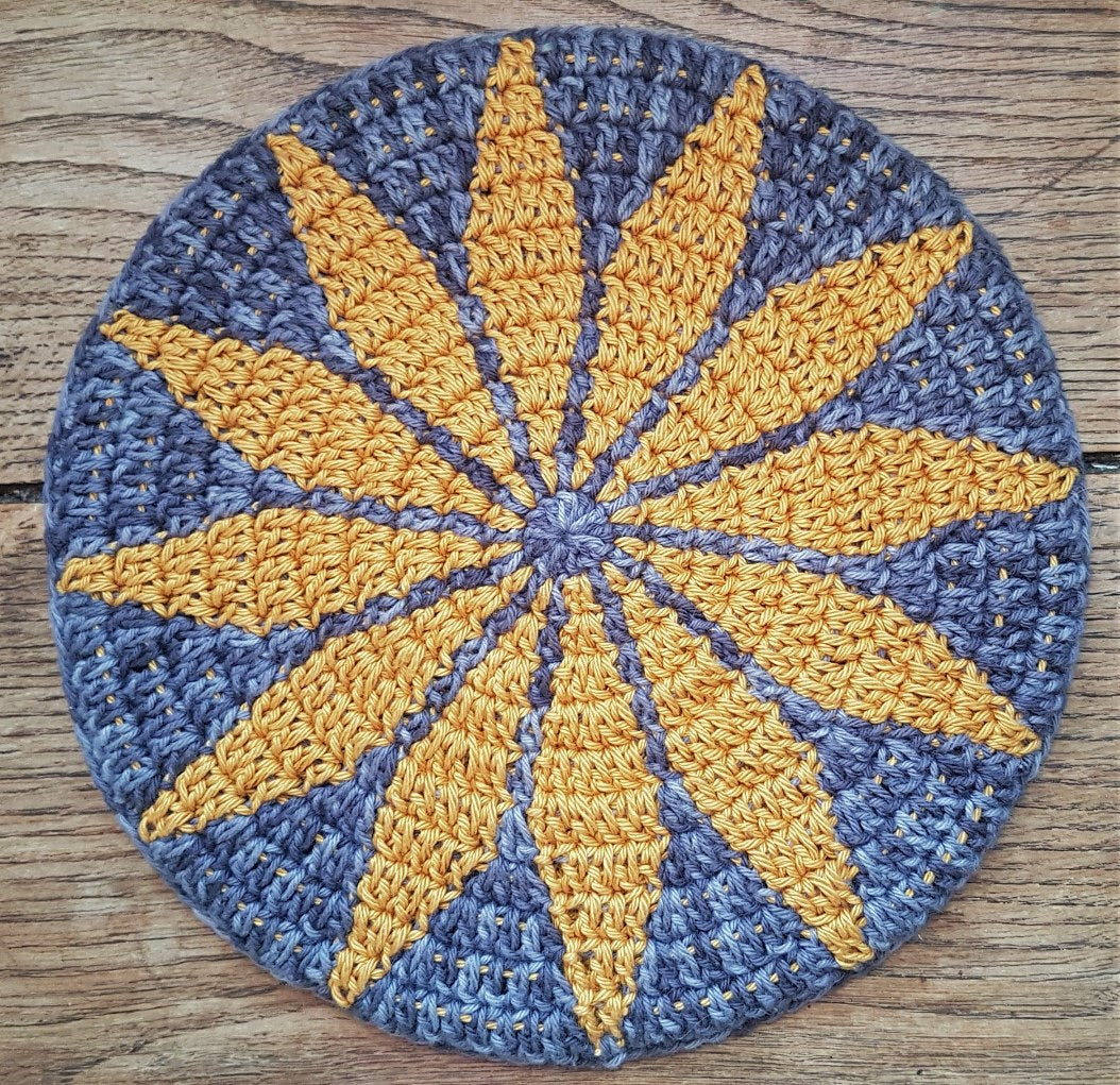Round crocheted mat with yellow star pattern on a wooden surface