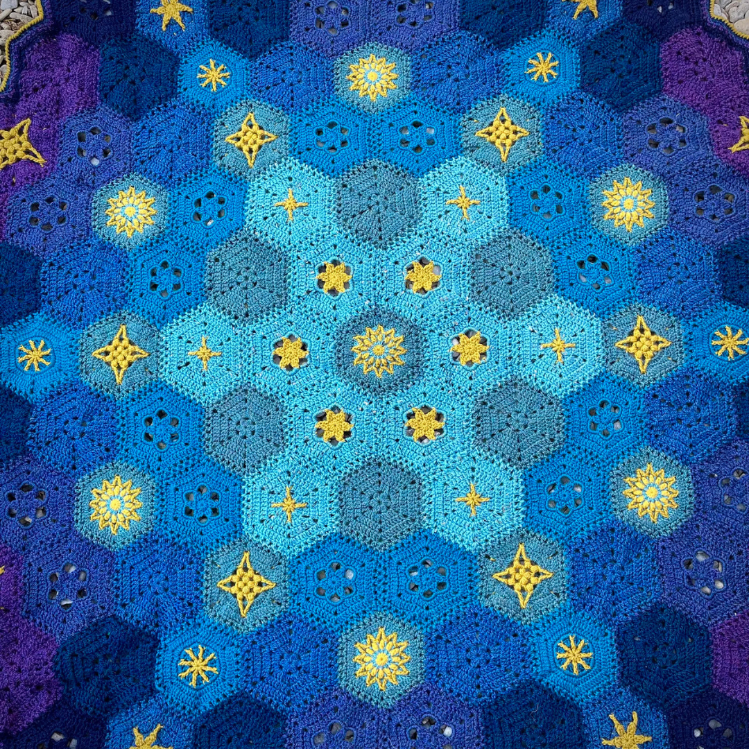 close-up of crochet star blanket with blue and purple colors and yellow star shapes.
