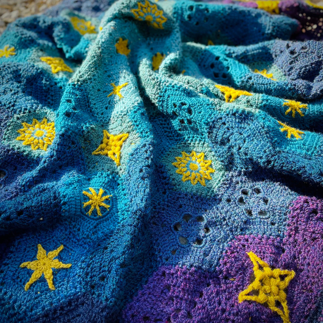 Close-up of a crocheted starlite blanket with star patterns in blue, purple, and yellow.