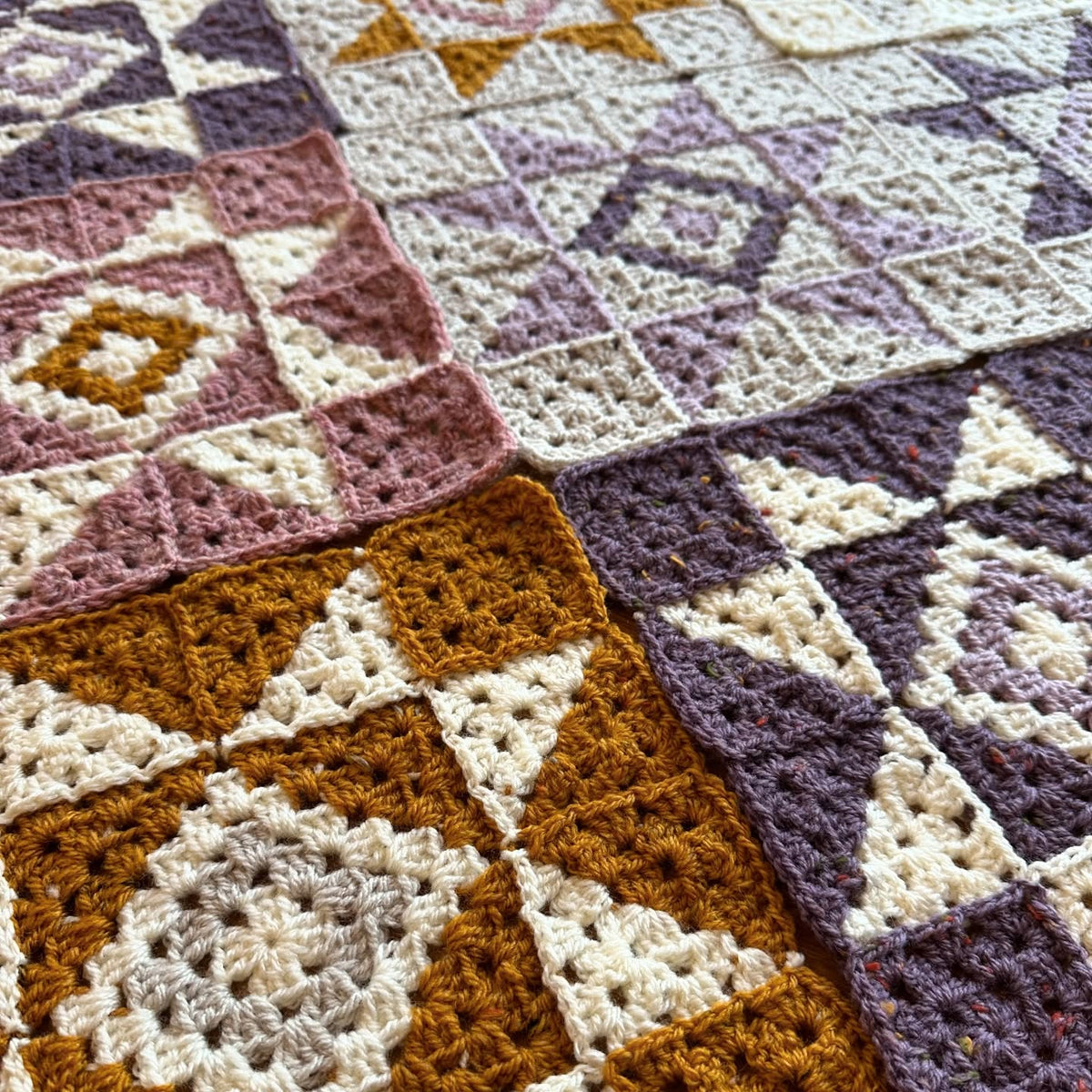 Close-up of a crocheted quiet sky blanket with geometric pattern in brown, purple, and white.