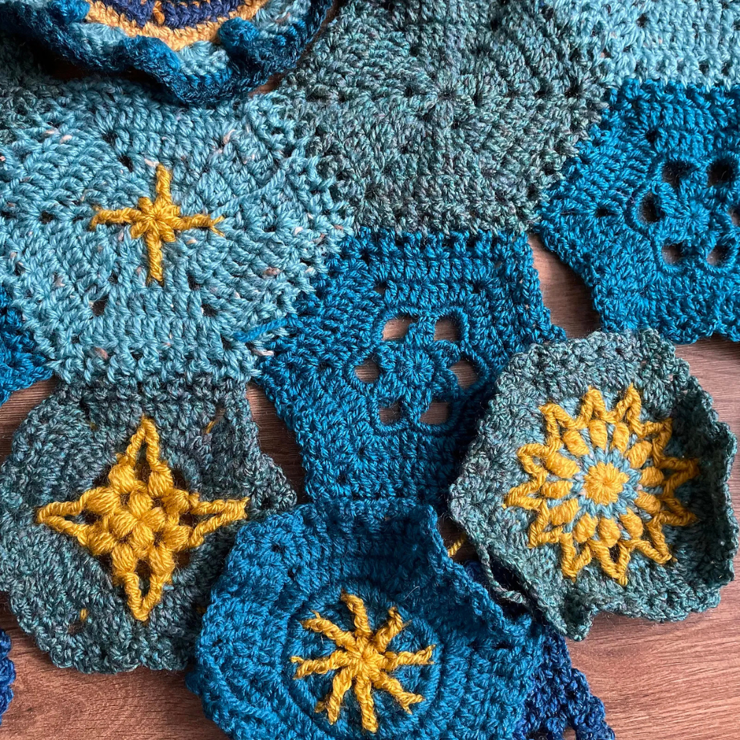 Blue crocheted squares with yellow star patterns on a wooden surface