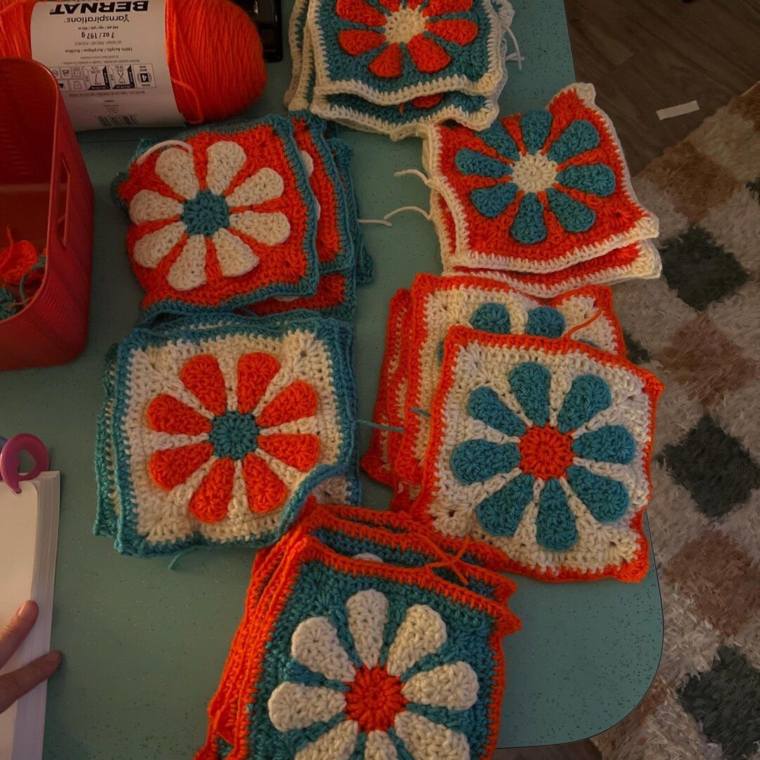 Colorful crocheted retro daisy granny squares on a table with yarn and tools.