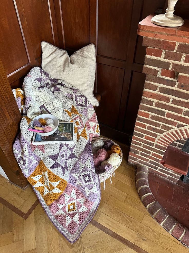 Crocheted quiet sky blanket draped over a wooden bench next to a brick fireplace.