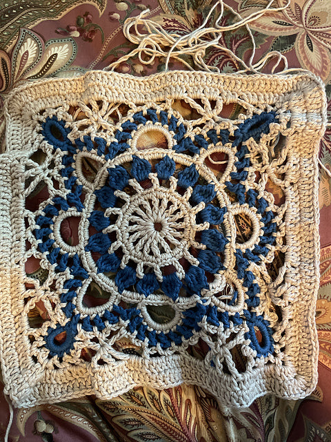 Crocheted turkish granny square with blue and beige pattern on a textured fabric background